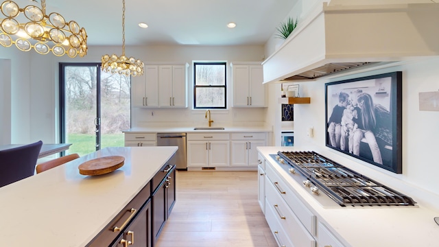 kitchen with a notable chandelier, stainless steel appliances, pendant lighting, sink, and white cabinetry