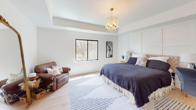 bedroom with a raised ceiling, light hardwood / wood-style floors, and an inviting chandelier