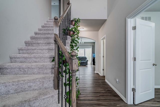 stairway with baseboards, visible vents, arched walkways, and wood finished floors