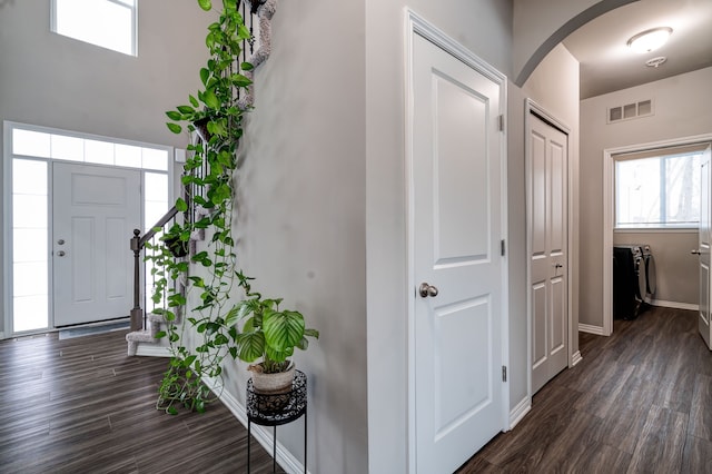 entryway with dark wood-style floors, arched walkways, visible vents, and baseboards