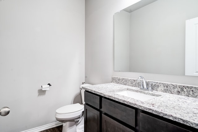 half bathroom with baseboards, vanity, toilet, and wood finished floors