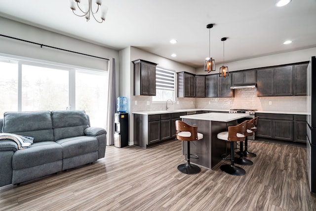 kitchen featuring a kitchen island, open floor plan, hanging light fixtures, light countertops, and dark brown cabinets