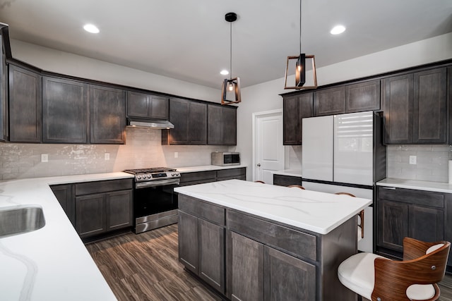 kitchen featuring decorative light fixtures, stainless steel appliances, dark wood-type flooring, dark brown cabinets, and under cabinet range hood