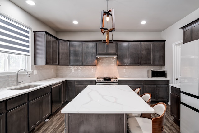 kitchen featuring appliances with stainless steel finishes, a center island, under cabinet range hood, pendant lighting, and a sink