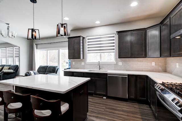 kitchen with stove, open floor plan, a sink, pendant lighting, and stainless steel dishwasher