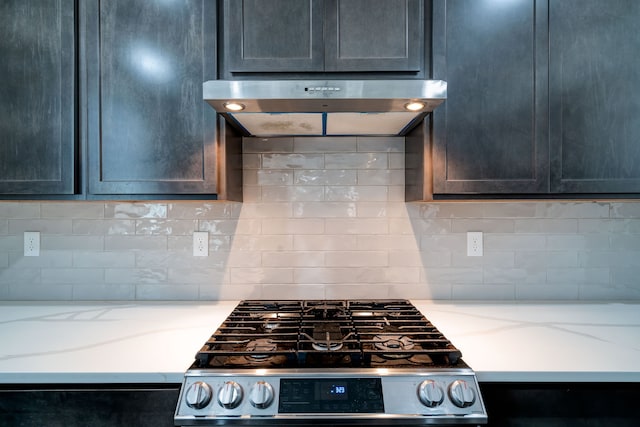 kitchen with light stone countertops, under cabinet range hood, tasteful backsplash, and gas range