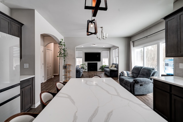 bedroom featuring dark wood-style floors, a fireplace, arched walkways, and baseboards