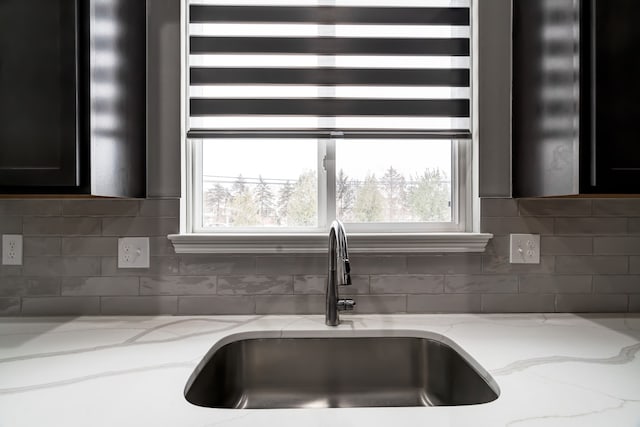 kitchen featuring tasteful backsplash, plenty of natural light, a sink, and light stone countertops