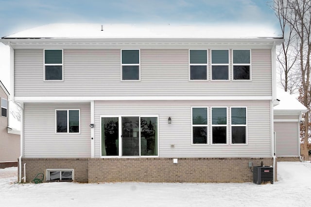 snow covered rear of property with central AC unit and brick siding