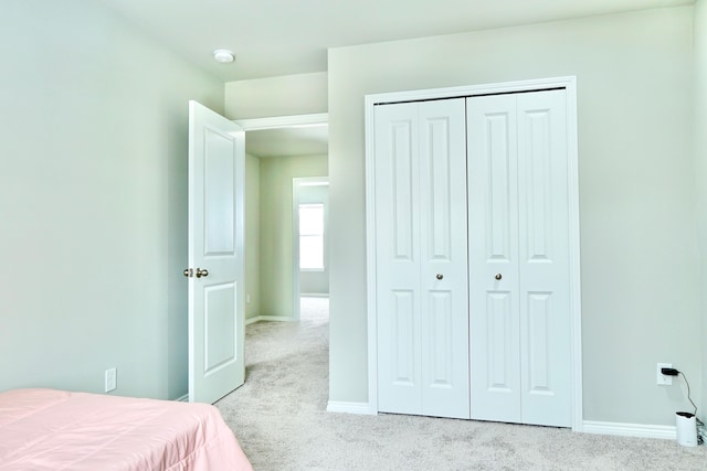 bedroom with baseboards, a closet, and light colored carpet