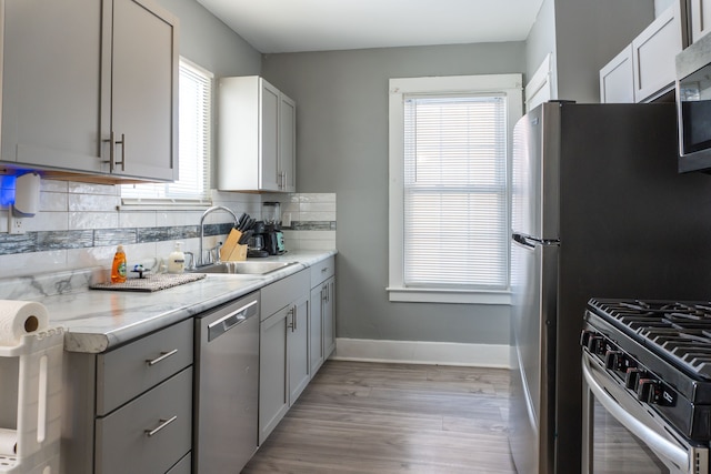 kitchen featuring a sink, appliances with stainless steel finishes, decorative backsplash, and gray cabinetry