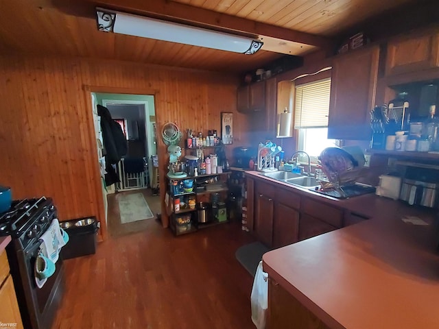 kitchen with sink, dark hardwood / wood-style flooring, stainless steel range with gas cooktop, wooden walls, and beam ceiling