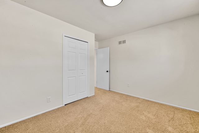 unfurnished bedroom with a closet, light carpet, visible vents, and baseboards