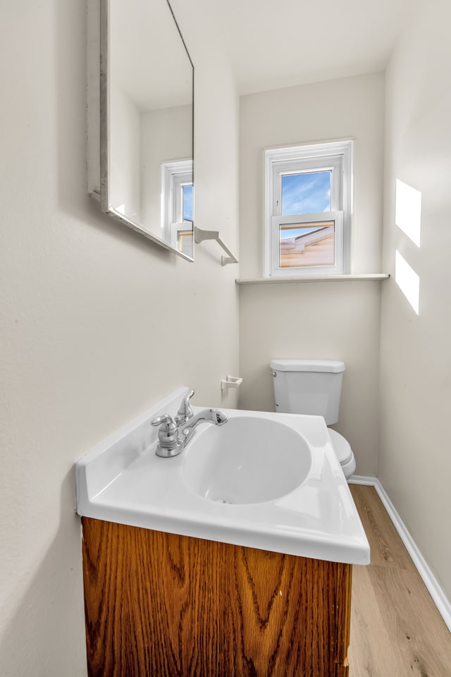 half bath featuring wood finished floors, a sink, toilet, and baseboards