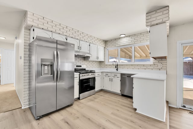 kitchen with light countertops, appliances with stainless steel finishes, white cabinetry, a sink, and under cabinet range hood