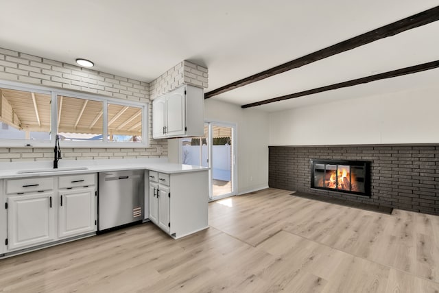 kitchen featuring dishwasher, light countertops, a brick fireplace, white cabinetry, and a sink