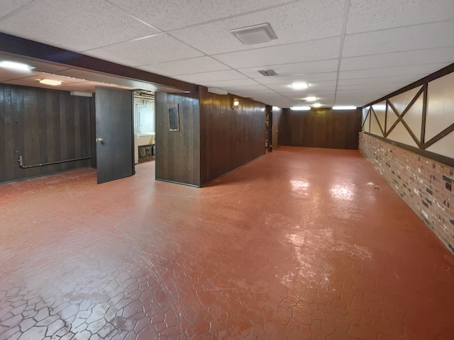 basement featuring a paneled ceiling and wood walls