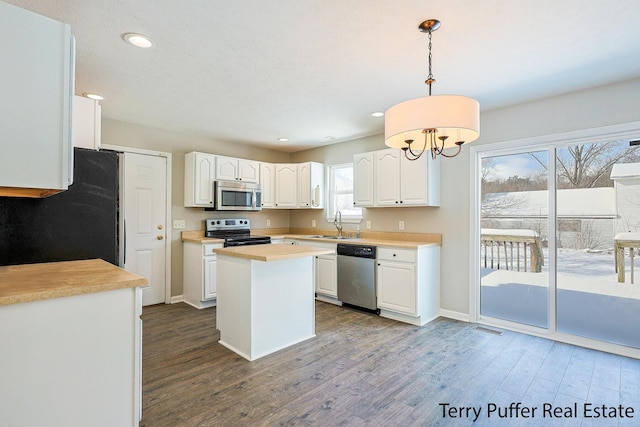 kitchen with appliances with stainless steel finishes, decorative light fixtures, hardwood / wood-style floors, a kitchen island, and white cabinetry