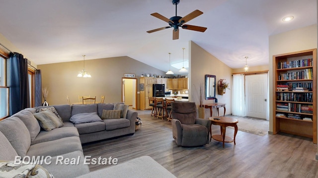 living room featuring ceiling fan with notable chandelier, vaulted ceiling, and wood finished floors