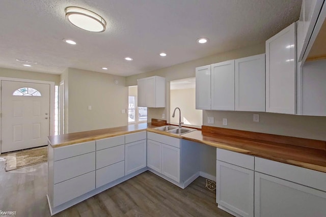 kitchen featuring light hardwood / wood-style flooring, sink, butcher block counters, kitchen peninsula, and white cabinets