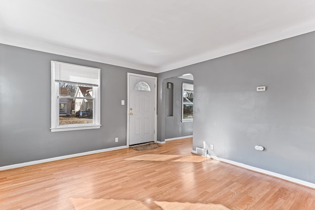 foyer entrance with arched walkways, baseboards, visible vents, and light wood-style floors