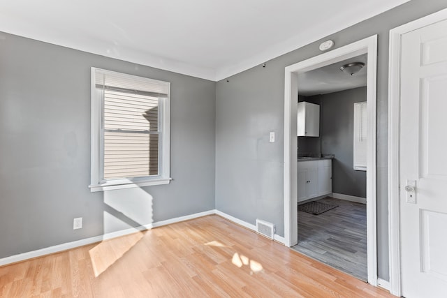 spare room with light wood finished floors, visible vents, and baseboards