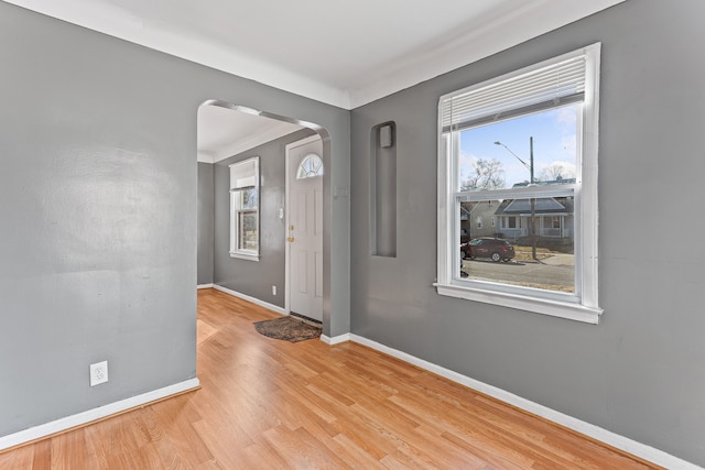 entrance foyer featuring light wood-style floors, arched walkways, and baseboards