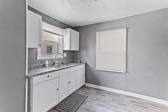 kitchen featuring light wood finished floors, baseboards, white cabinets, and a sink