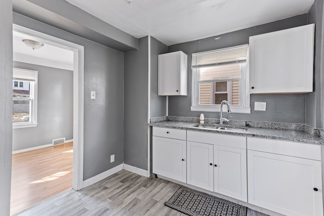 kitchen featuring white cabinetry, a sink, visible vents, and light wood finished floors