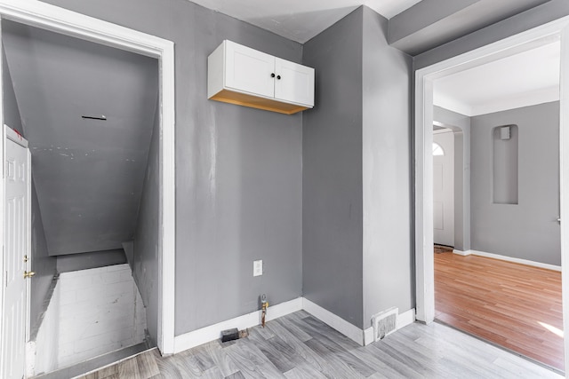 laundry room with light wood-style floors, arched walkways, visible vents, and baseboards