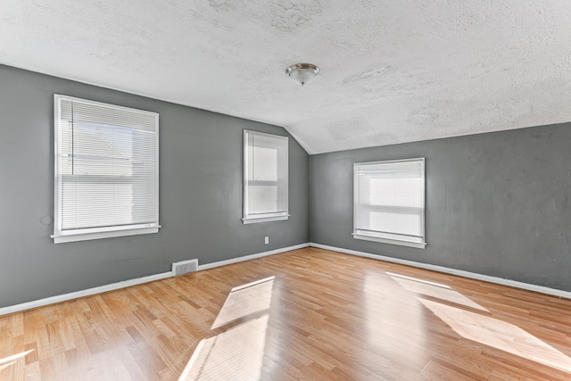 empty room with baseboards, visible vents, vaulted ceiling, and wood finished floors