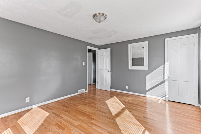 spare room featuring a textured ceiling, light wood-style flooring, visible vents, and baseboards