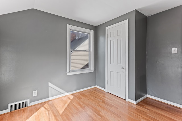 unfurnished bedroom featuring visible vents, vaulted ceiling, baseboards, and wood finished floors