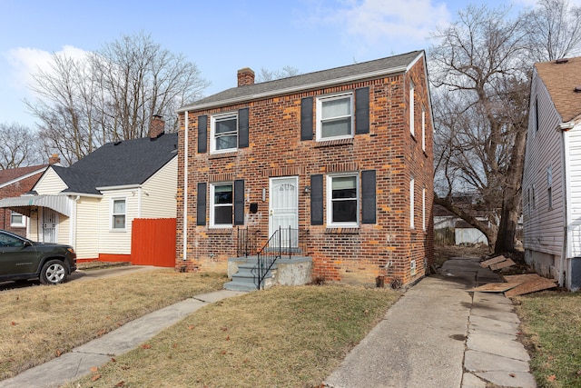 view of front facade featuring brick siding, a chimney, and a front lawn