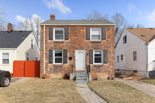 colonial house with brick siding, a chimney, a front yard, and fence