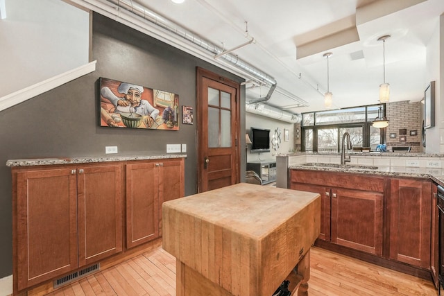 kitchen featuring light hardwood / wood-style floors, pendant lighting, sink, and light stone countertops