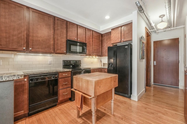 kitchen with light hardwood / wood-style flooring, backsplash, light stone counters, pendant lighting, and black appliances