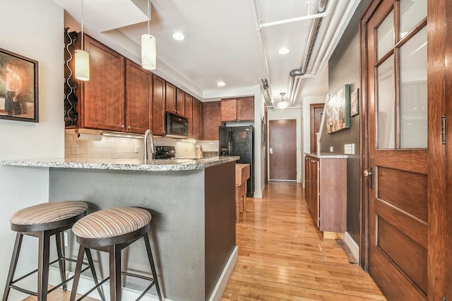 kitchen featuring backsplash, black appliances, a breakfast bar, and light hardwood / wood-style flooring