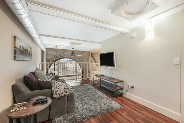 living room featuring brick wall, dark wood-type flooring, beamed ceiling, and ceiling fan