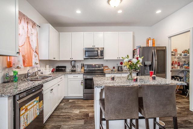 kitchen with stainless steel appliances, light stone countertops, a center island, sink, and white cabinetry