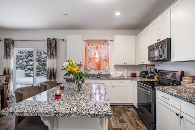 kitchen with dark stone countertops, a center island, white cabinetry, and black appliances