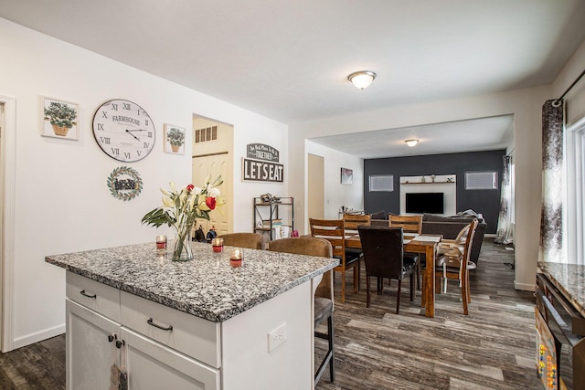 kitchen featuring a center island, a breakfast bar, light stone counters, white cabinets, and dark hardwood / wood-style floors