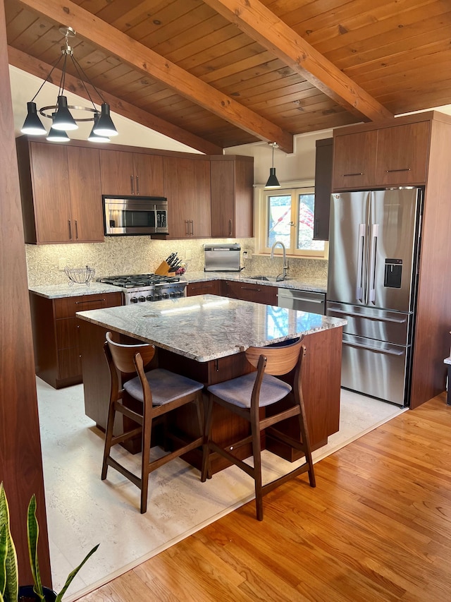 kitchen with appliances with stainless steel finishes, pendant lighting, a kitchen island, and sink