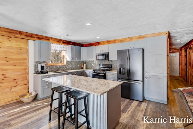 kitchen with appliances with stainless steel finishes, decorative backsplash, light hardwood / wood-style floors, a breakfast bar, and a center island