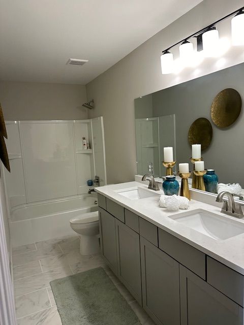 full bathroom featuring double vanity, marble finish floor,  shower combination, and a sink