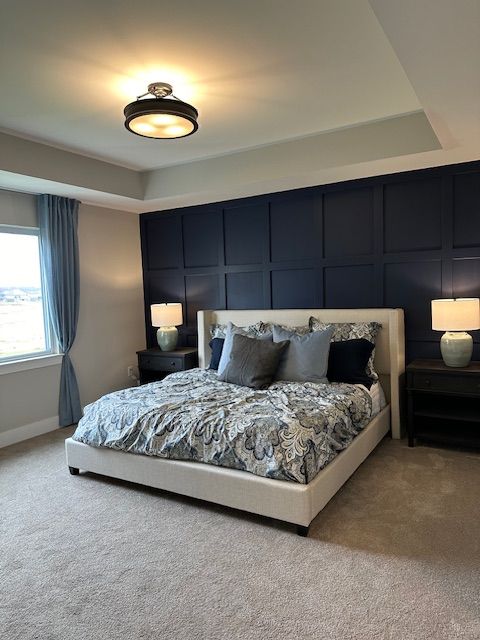 bedroom featuring baseboards, a decorative wall, and light colored carpet
