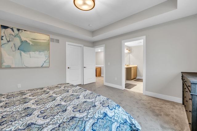 carpeted bedroom with a raised ceiling and ensuite bathroom