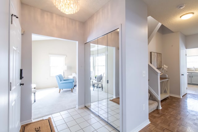 hall featuring light tile patterned floors, a textured ceiling, a chandelier, baseboards, and stairs