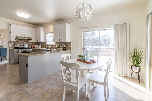 kitchen featuring stainless steel range with gas cooktop, pendant lighting, white cabinets, under cabinet range hood, and a peninsula