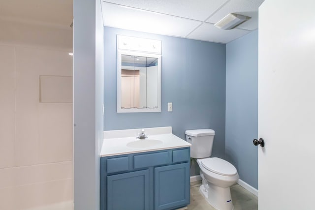 full bath featuring a drop ceiling, toilet, vanity, baseboards, and walk in shower